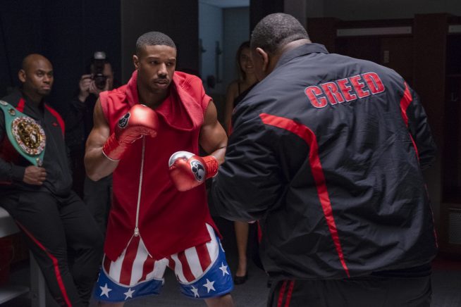 A young African American boxer wearing the colours of the American flag trains with a heavy-set man with the word 'Creed II' on the back of his training gear.
