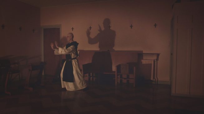 A priest seems to carry out a martial arts pose in his full robes in a mysteriously dark lit room in this still from Underwire Film Festival's Lovers of the Night.