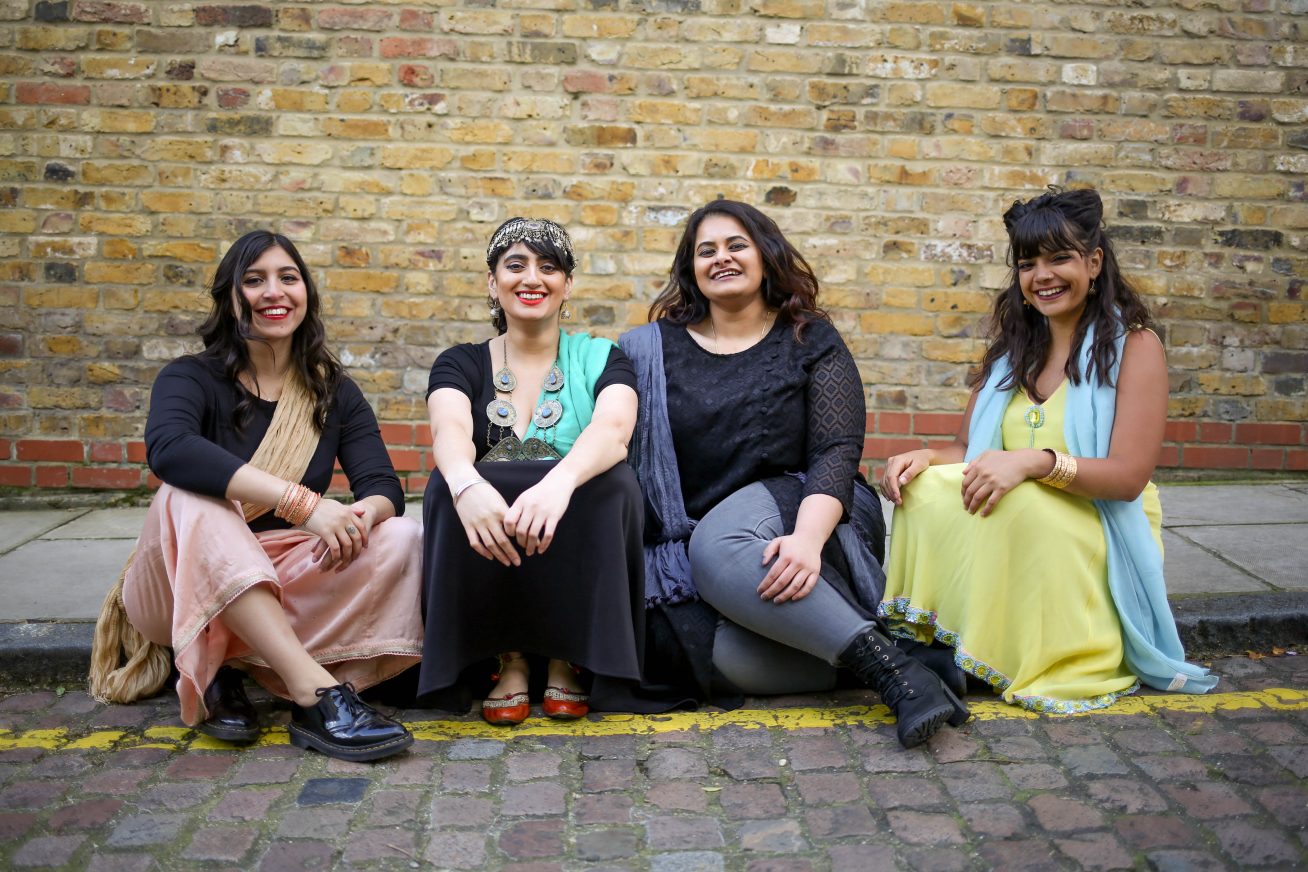 4 womxn sit side by side, dressed in South Asian attire