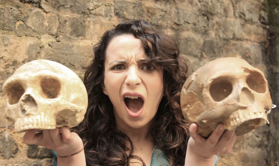 A woman pulls a funny face as she holds two skulls up to the camera