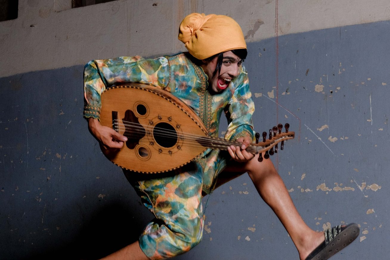 A person jumps in the air whilst smiling and playing a guitar-like instrument