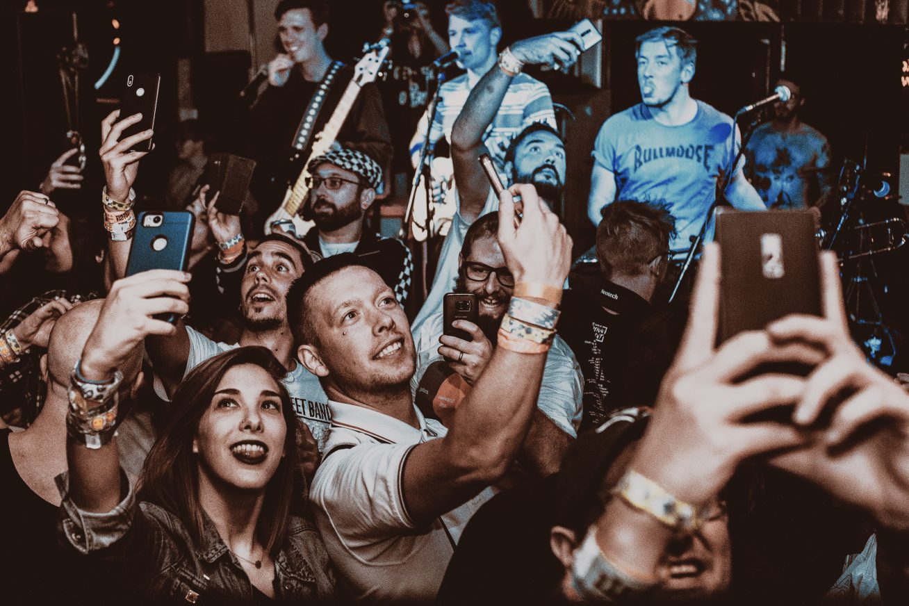 A busy gig audience hold up their phones to take photos of the band, Ghouls, who are performing on stage