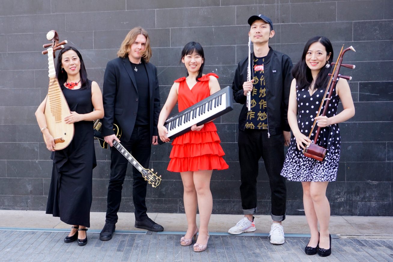 A band pose in front of a black wall with their various instruments