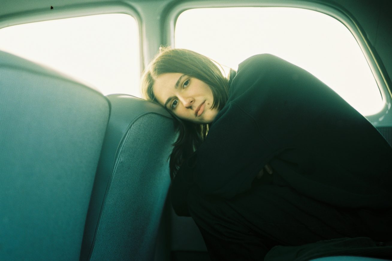A woman sits in the back seat of a car resting her head on the seat in front of her