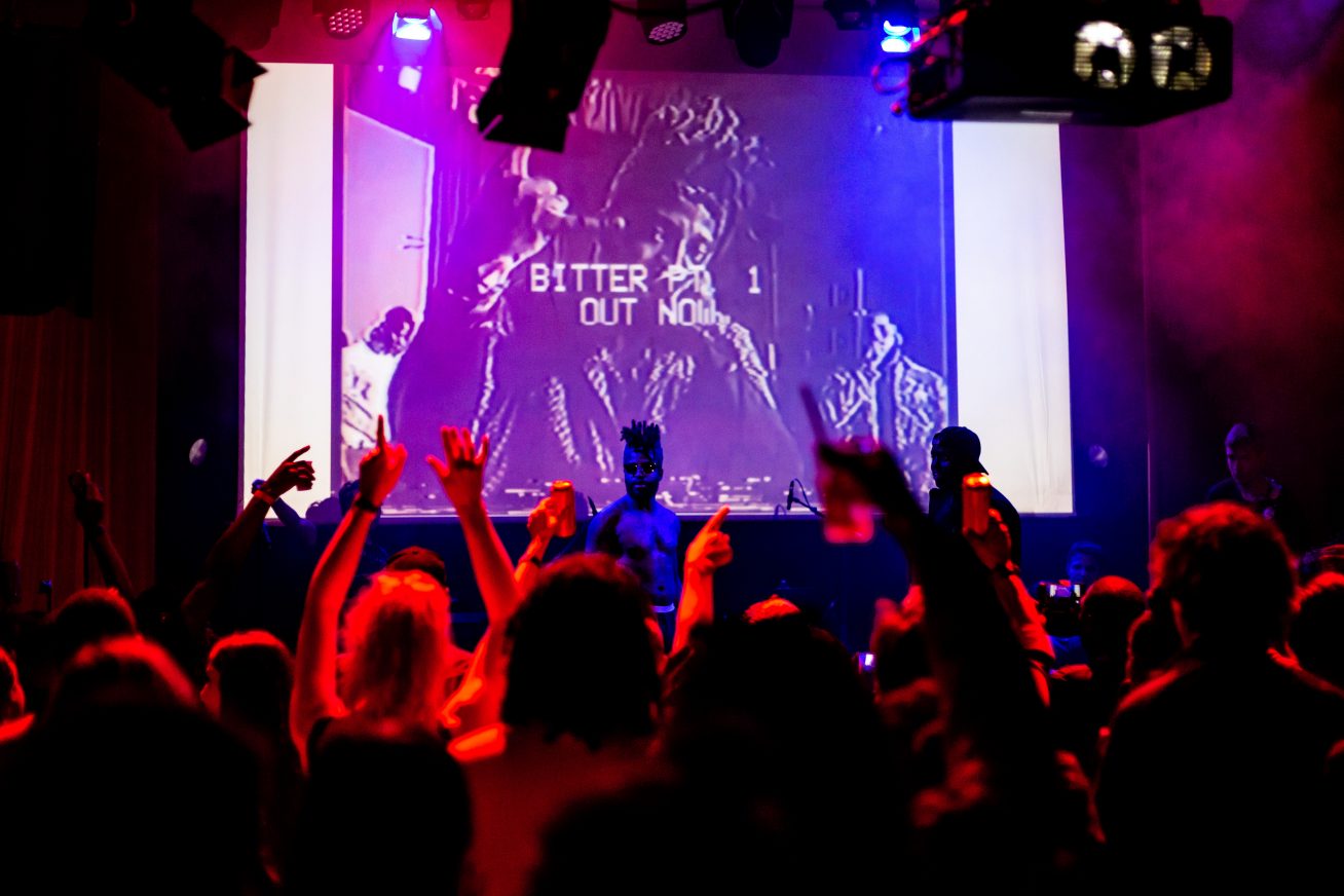 The crowd raise their hands as artists perform on stage at a gig