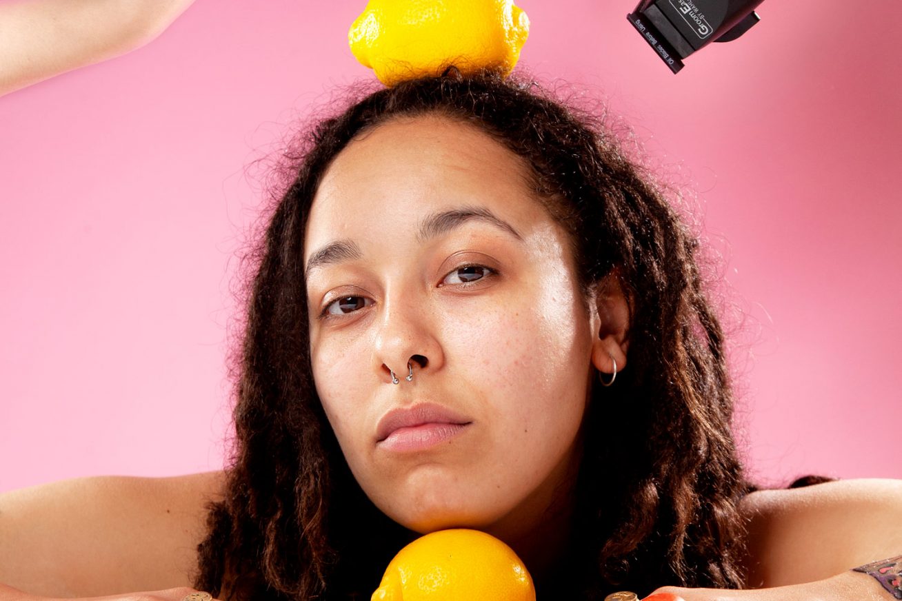 A person poses with lemons against a pink background