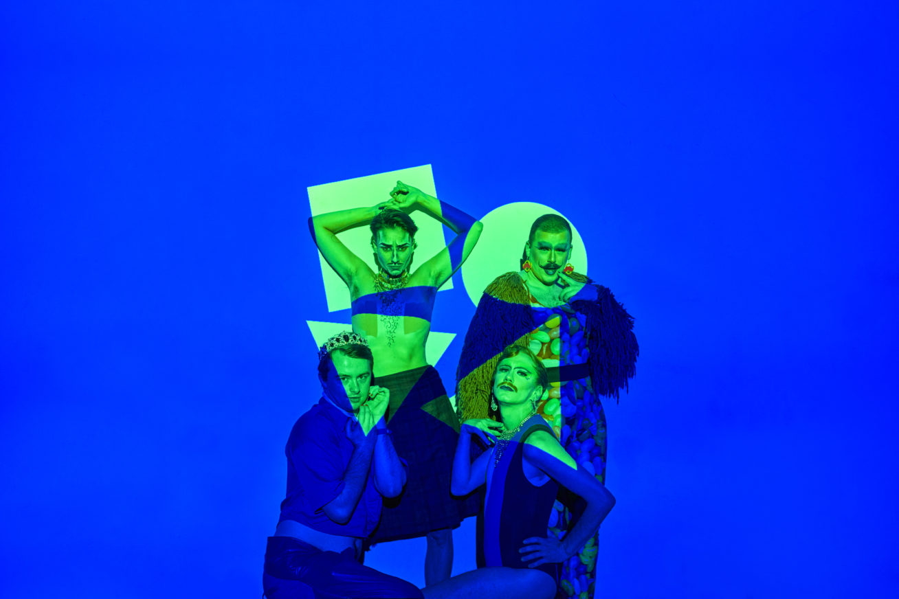 four non-binary people posing against a blue background, faces highlighted in neon